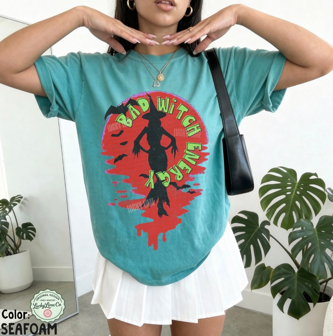 Person wearing a teal t-shirt with a graphic design and white skirt indoors.