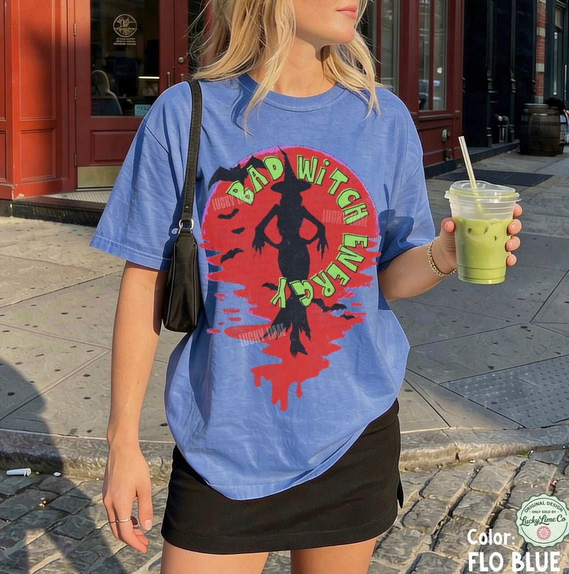 Person wearing a blue t-shirt with a graphic design, holding a drink on a street.