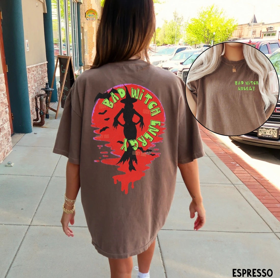 Person wearing a brown t-shirt with a colorful graphic and text on the back, standing on a sidewalk.