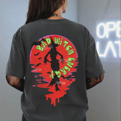 Person wearing a t-shirt with a colorful graphic design on the back, standing in front of a neon sign.