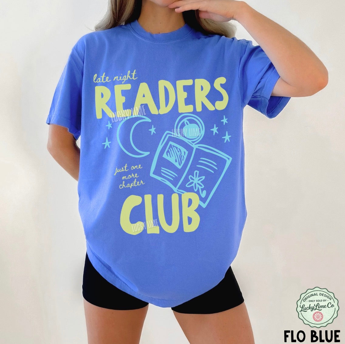 Person wearing a blue t-shirt with 'Late Night Readers Club' text and graphics on a plain background