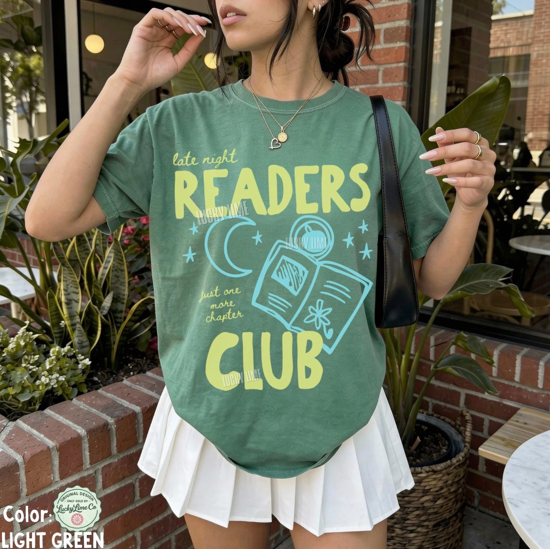 Person wearing a green t-shirt with 'Late Night Readers Club' design outdoors.