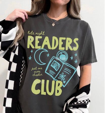 Person wearing a dark gray t-shirt with 'Late Night Readers Club' design, holding a black and white checkered jacket.
