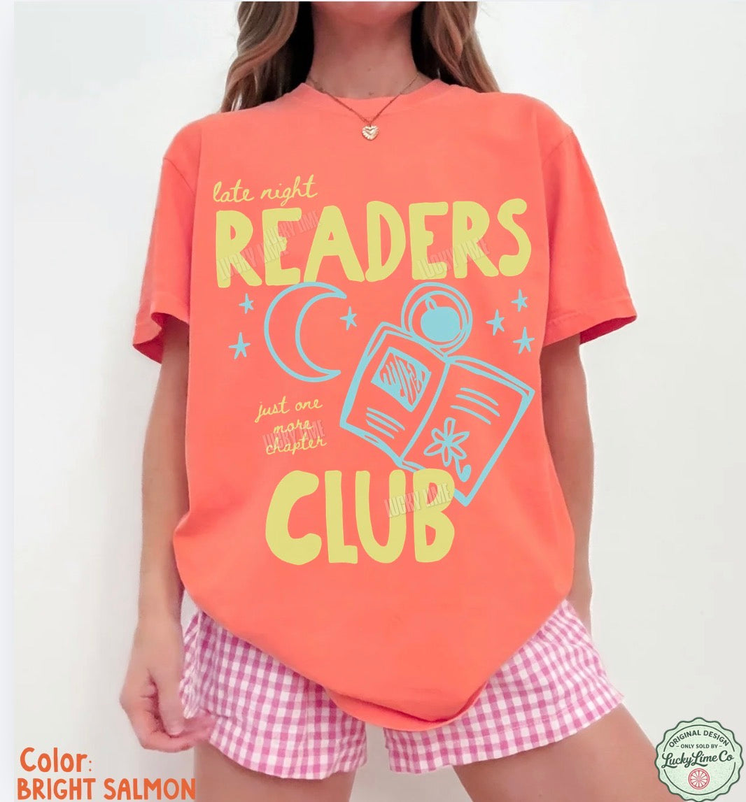Person wearing a bright salmon t-shirt with 'Readers Club' design and pink checkered shorts on a white background.