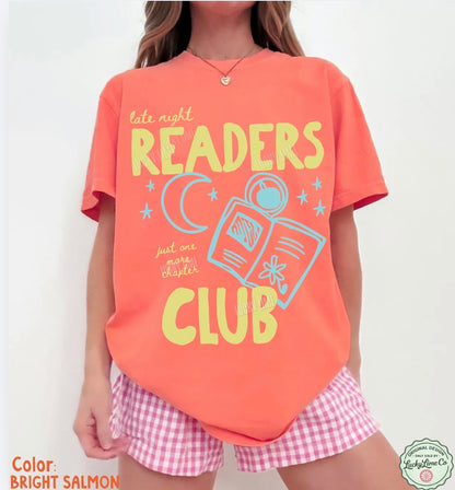 Person wearing a bright salmon t-shirt with 'Readers Club' design and pink checkered shorts on a white background.