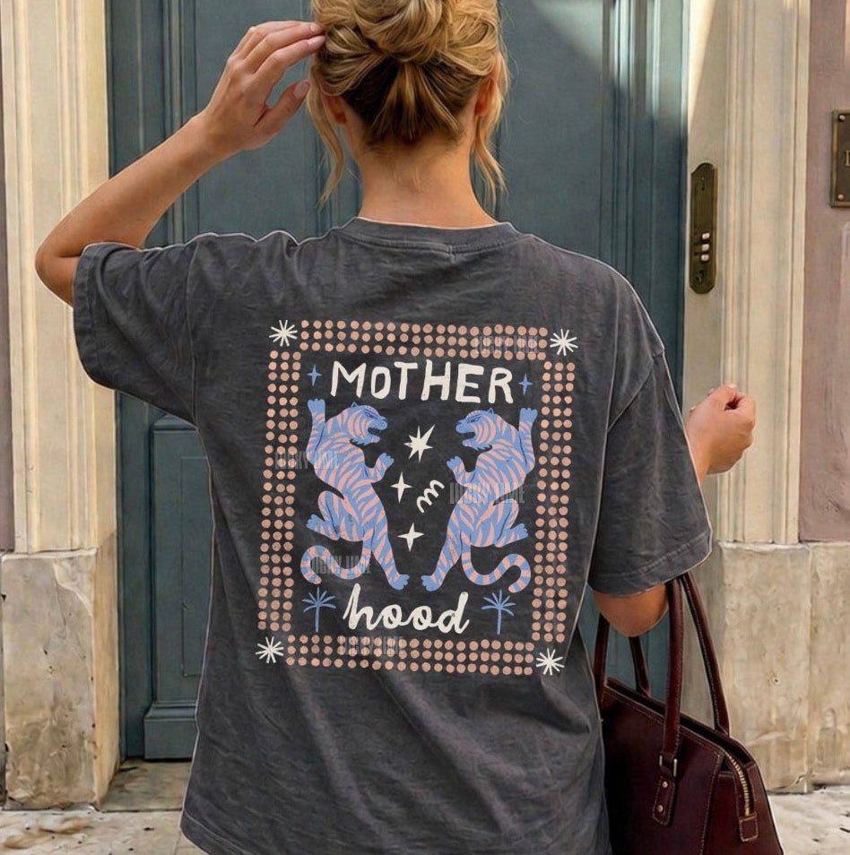 Person wearing a t-shirt with 'Motherhood' design, standing in front of a building.