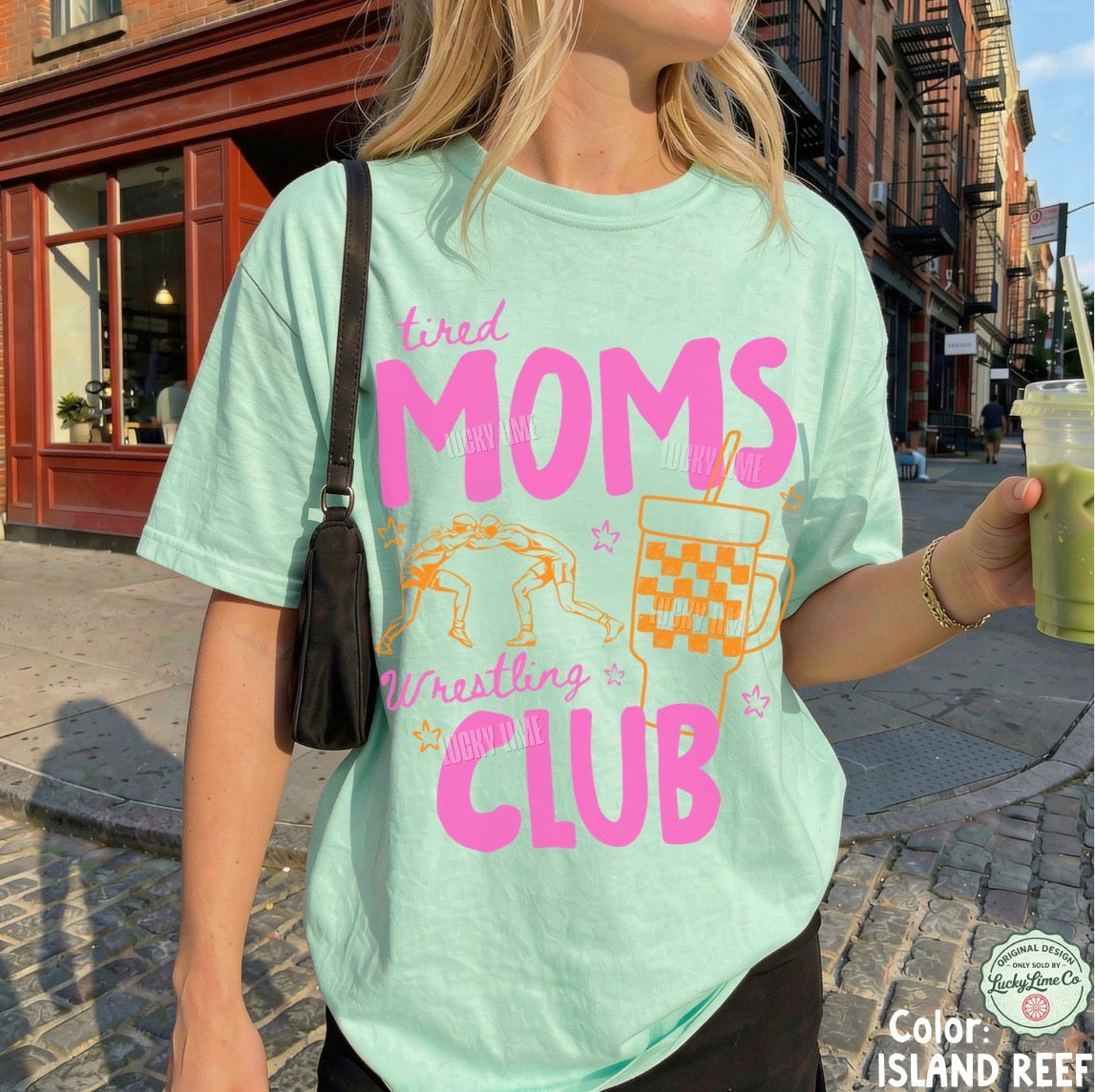 Person wearing a light green t-shirt with pink and orange text and graphics, standing on a street.