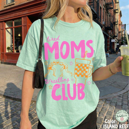 Person wearing a light green t-shirt with pink and orange text and graphics, standing on a street.