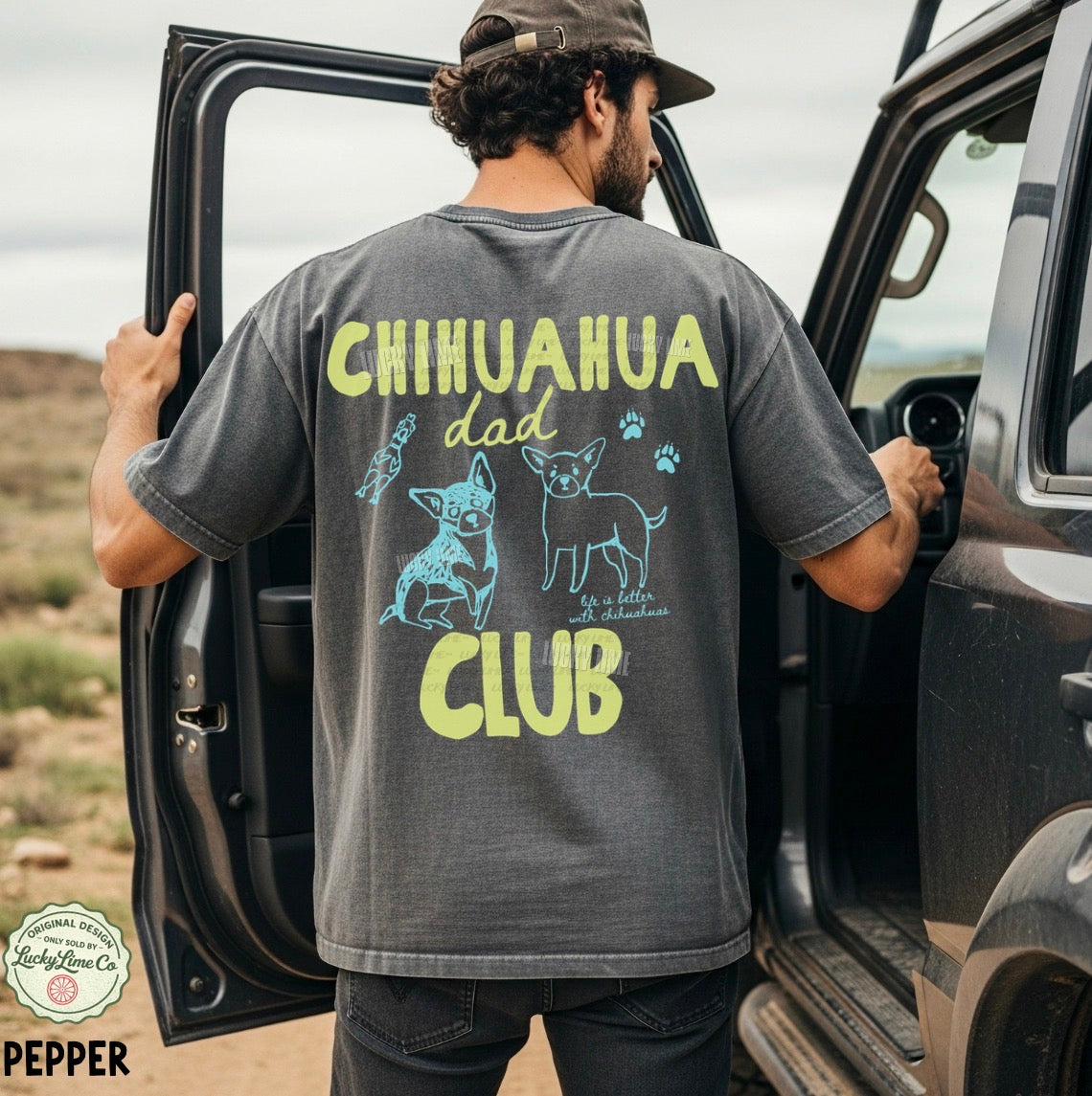 Man wearing a t-shirt with 'Chihuahua Dad Club' design, standing next to an open car door in a desert setting.