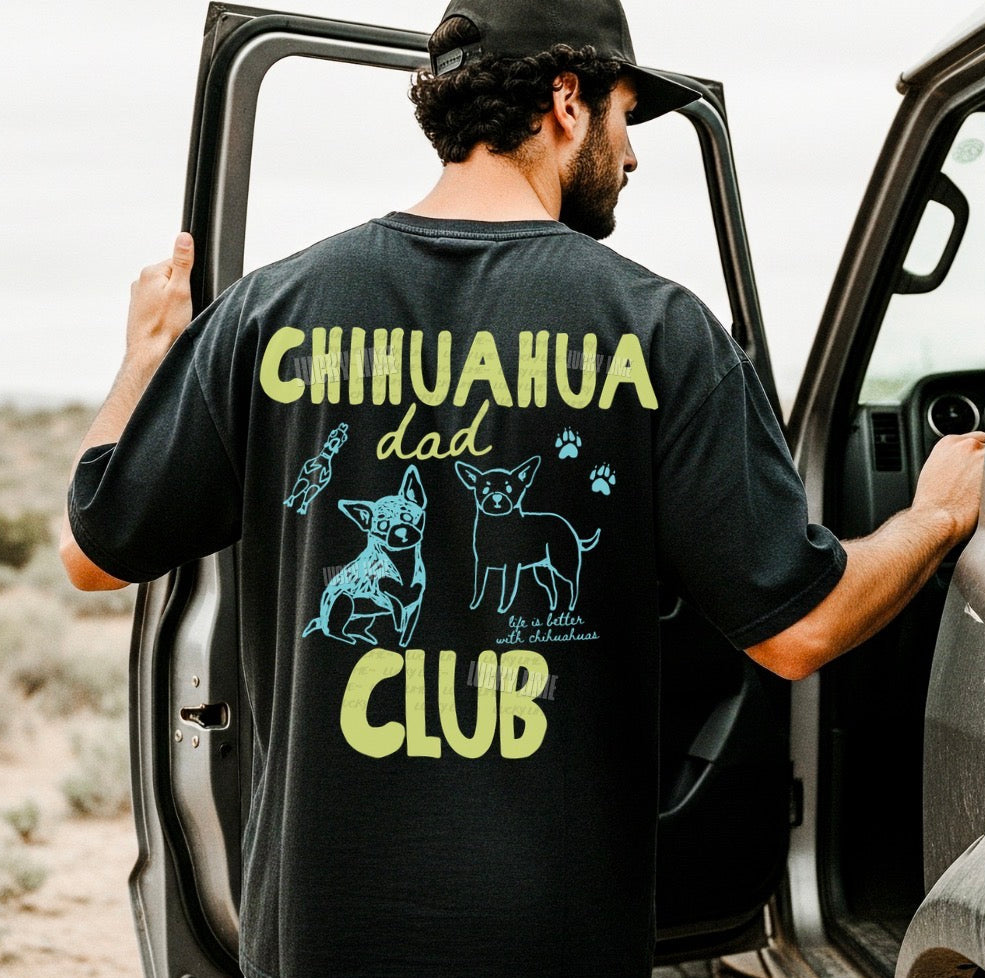 Man wearing a black t-shirt with 'Chihuahua dad club' design, standing next to an open car door in a desert setting.