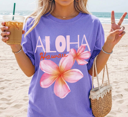Person wearing a purple 'Aloha Hawaii' t-shirt with floral designs on a beach.