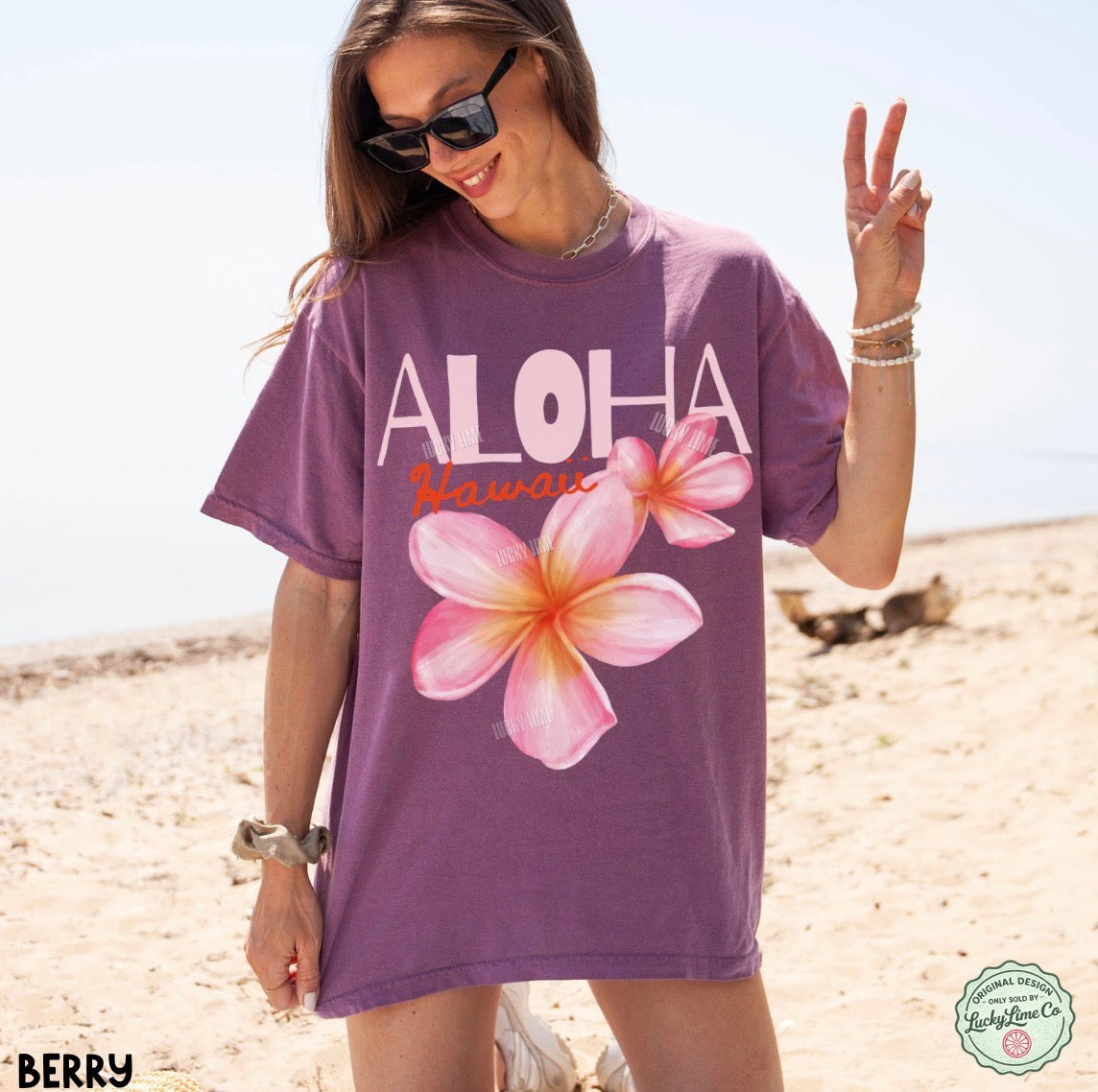 Woman wearing a purple 'Aloha Hawaii' t-shirt with floral designs on a beach.