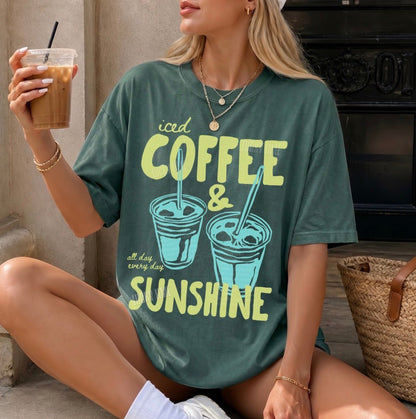 Woman wearing a green t-shirt with 'iced coffee & sunshine' design, holding a drink.