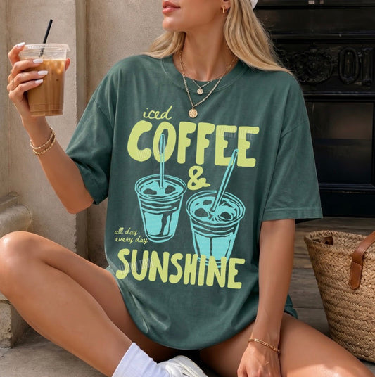 Woman wearing a green t-shirt with 'iced coffee & sunshine' design, holding a drink.
