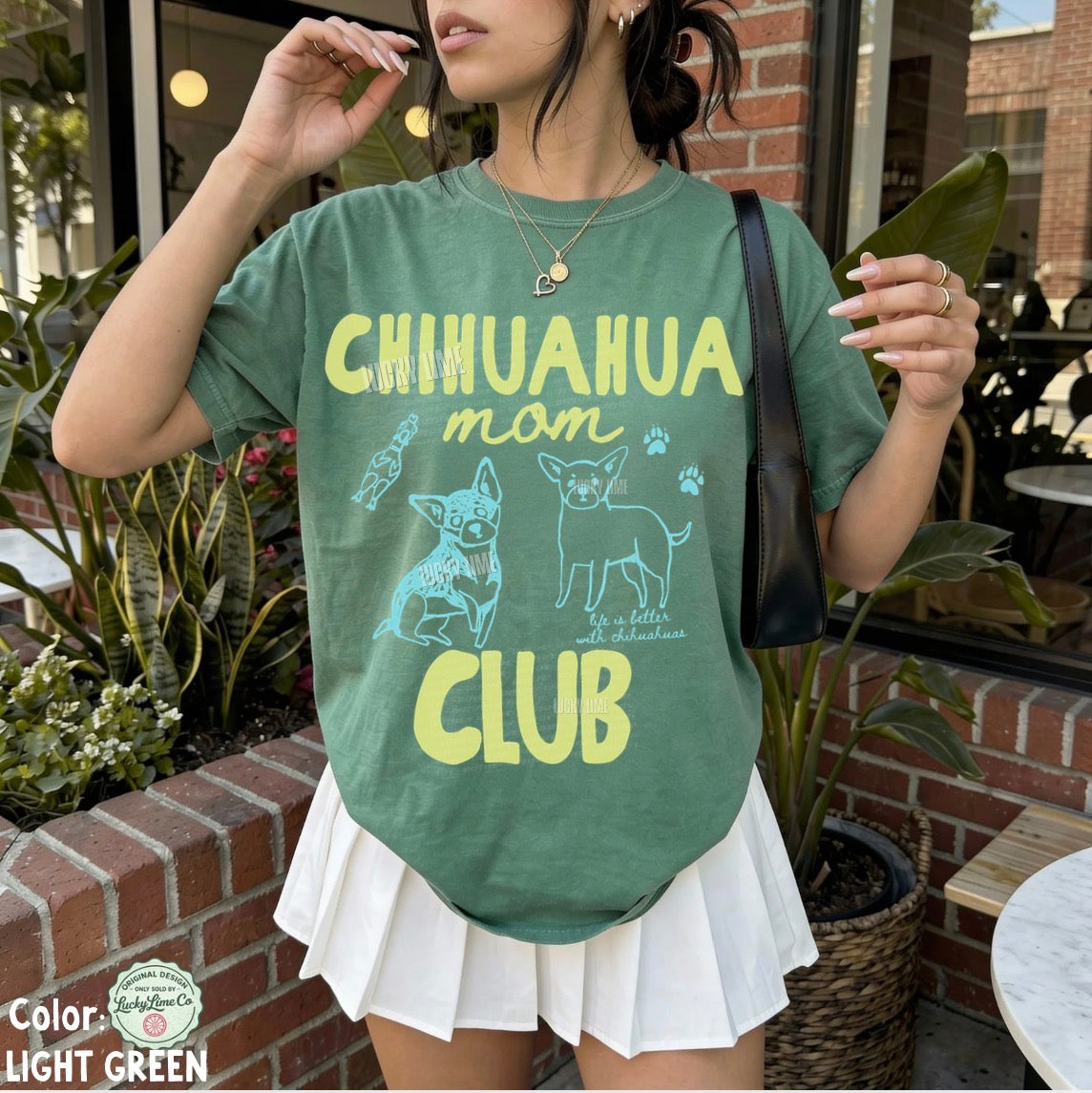 Person wearing a green t-shirt with 'Chihuahua mom club' text and graphics outdoors.