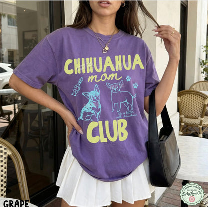 Person wearing a purple t-shirt with 'Chihuahua mom club' text and graphics, standing outdoors.