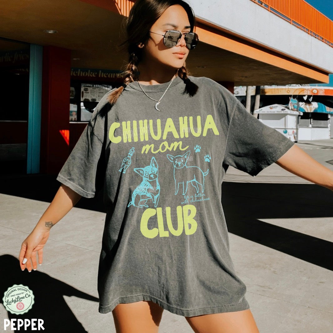 Woman wearing a gray t-shirt with 'Chihuahua mom club' text and graphics outdoors.
