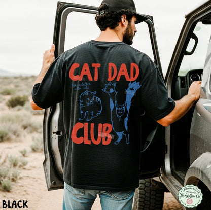 Man wearing a black t-shirt with 'Cat Dad Club' text and graphics, standing next to an open car door in a desert setting.