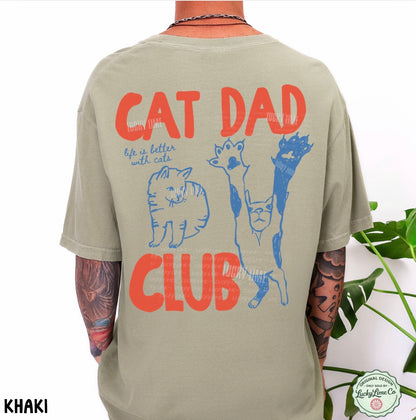 Khaki t-shirt with 'Cat Dad Club' text and cat illustrations on the back, worn by a person with tattoos.