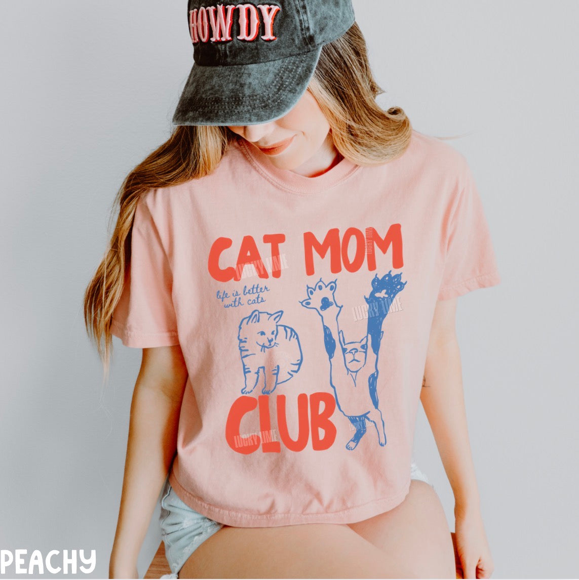 Person wearing a pink t-shirt with 'Cat Mom Club' design and a cap.