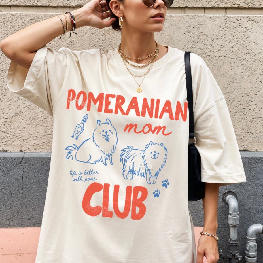 Person wearing a 'Pomeranian mom club' t-shirt against a wall.