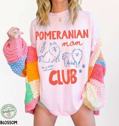 Person wearing a pink sweatshirt with 'Pomeranian mom club' text and graphics, holding a colorful knit item.