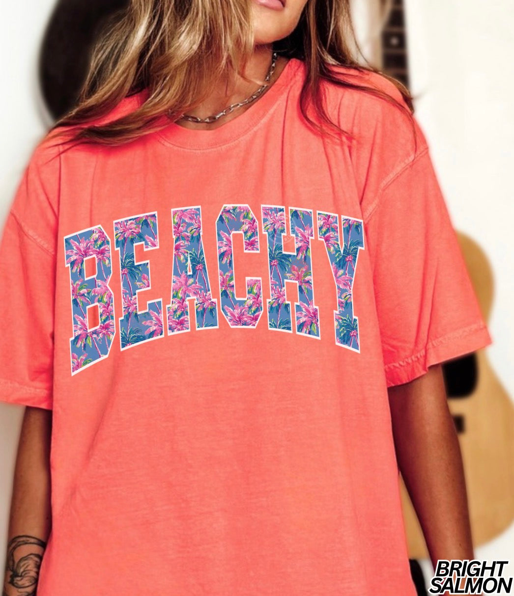 Coral t-shirt with 'BEACHY' text in floral letters worn by a person.