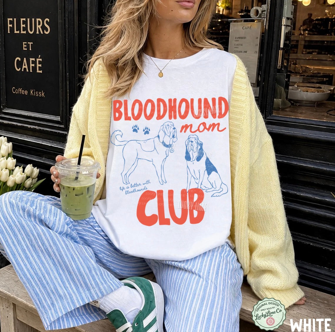 Person wearing a 'Bloodhound mom club' shirt sitting in front of a cafe.