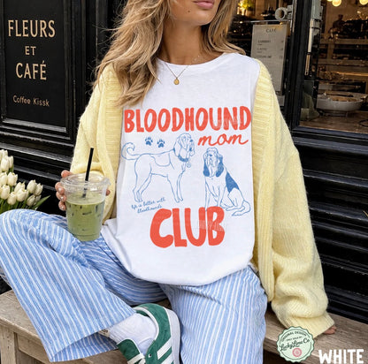 Person wearing a 'Bloodhound mom club' shirt sitting in front of a cafe.