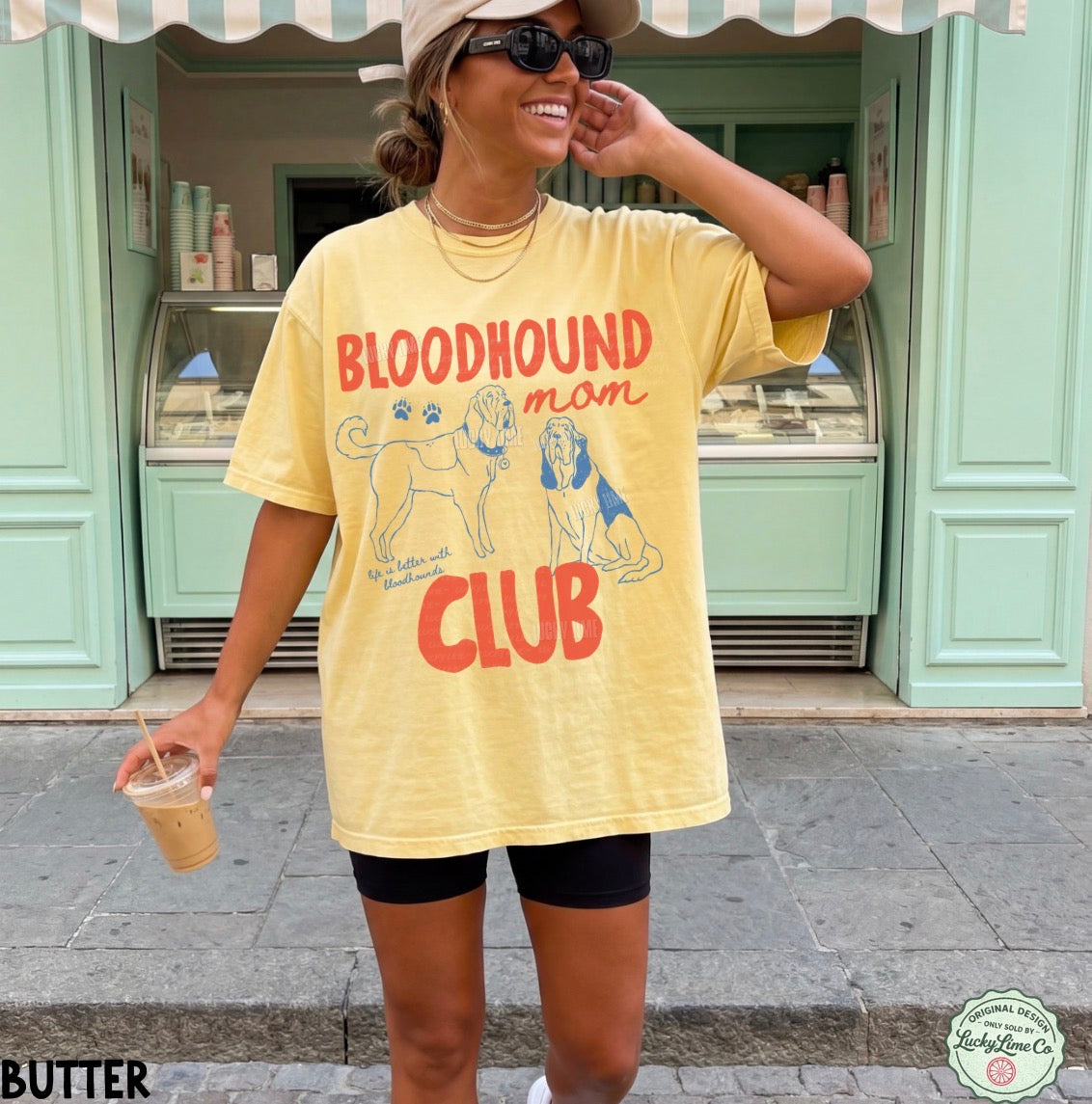 Person wearing a yellow 'Bloodhound Mom Club' t-shirt in front of a store.