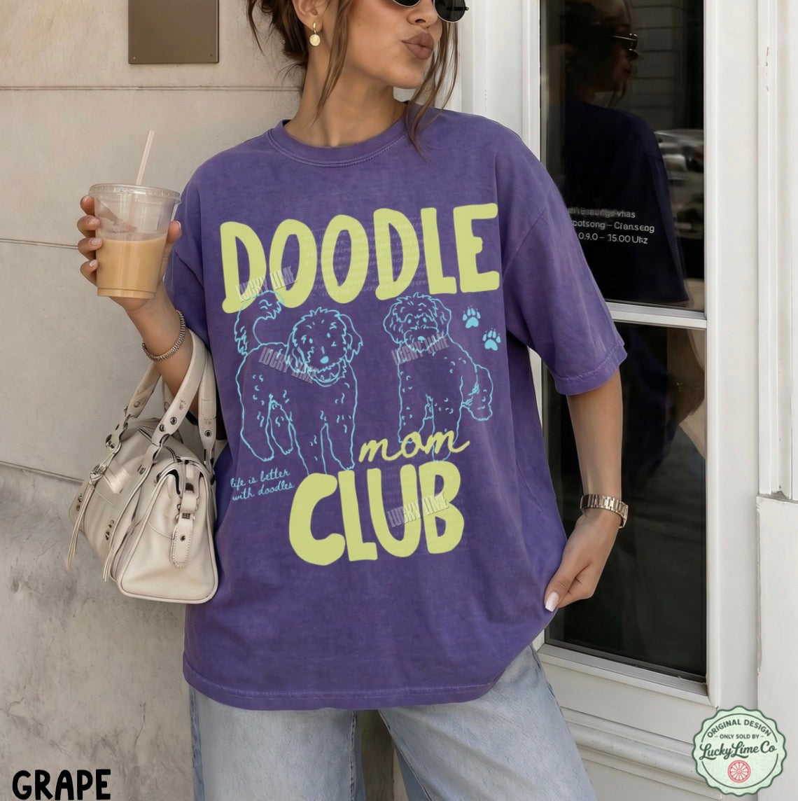 Person wearing a purple 'Doodle Mom Club' t-shirt holding a drink.