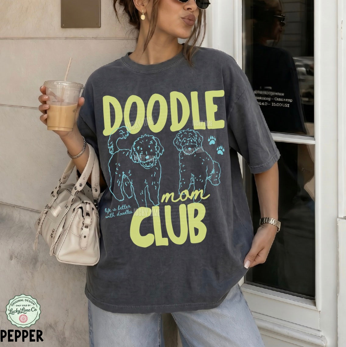 Person wearing a 'Doodle Mom Club' t-shirt holding a drink.