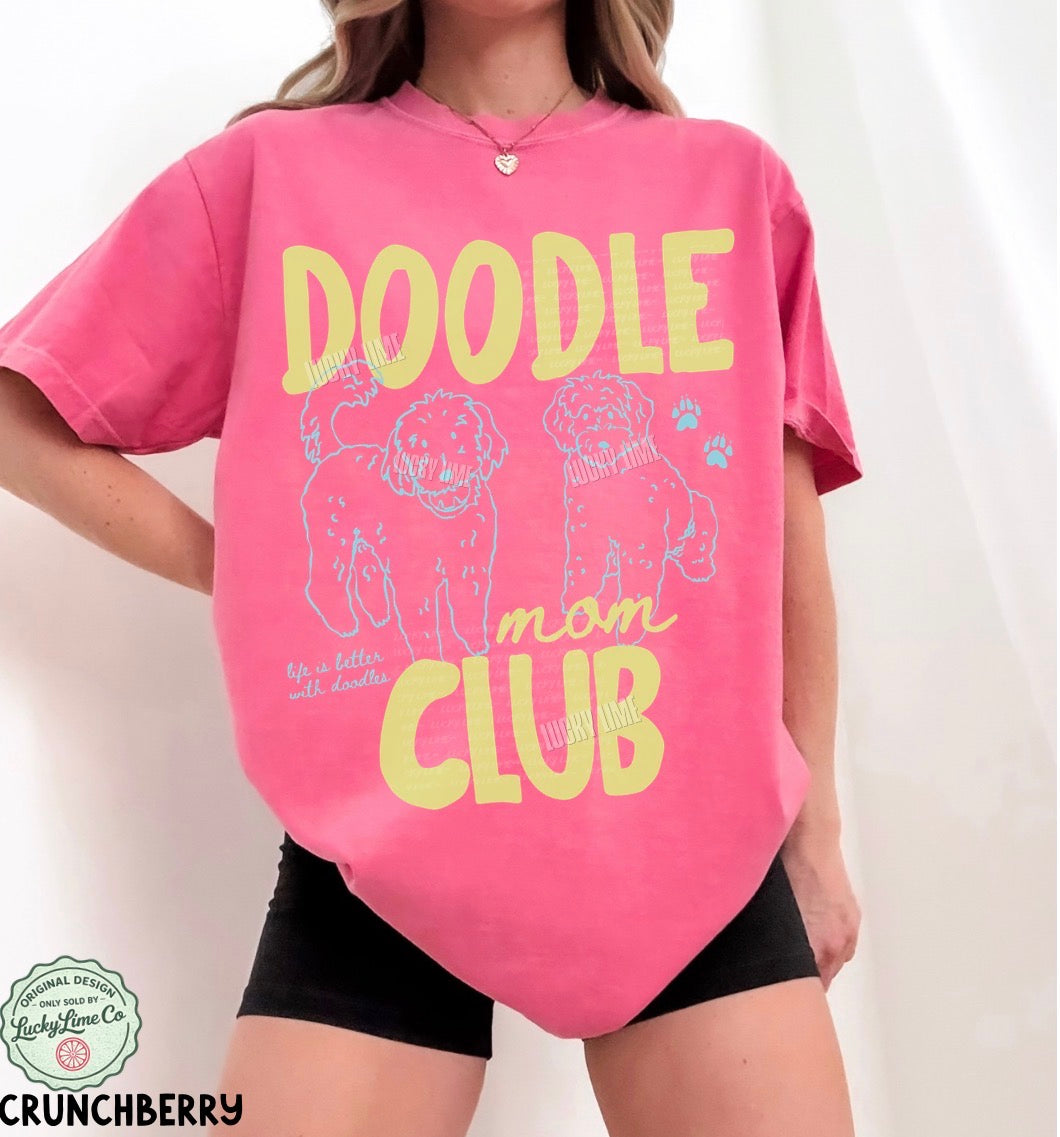 Person wearing a pink t-shirt with 'Doodle Mom Club' text and dog illustrations on a white background.