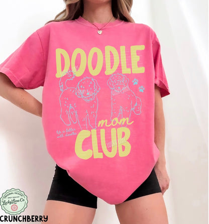 Person wearing a pink t-shirt with 'Doodle Mom Club' text and dog illustrations on a white background.