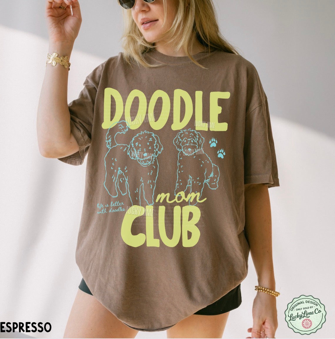Person wearing a brown t-shirt with 'Doodle Mom Club' text and dog illustrations on a light background.