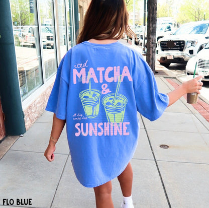 Person wearing a blue oversized t-shirt with 'iced matcha & sunshine' text on a sidewalk.