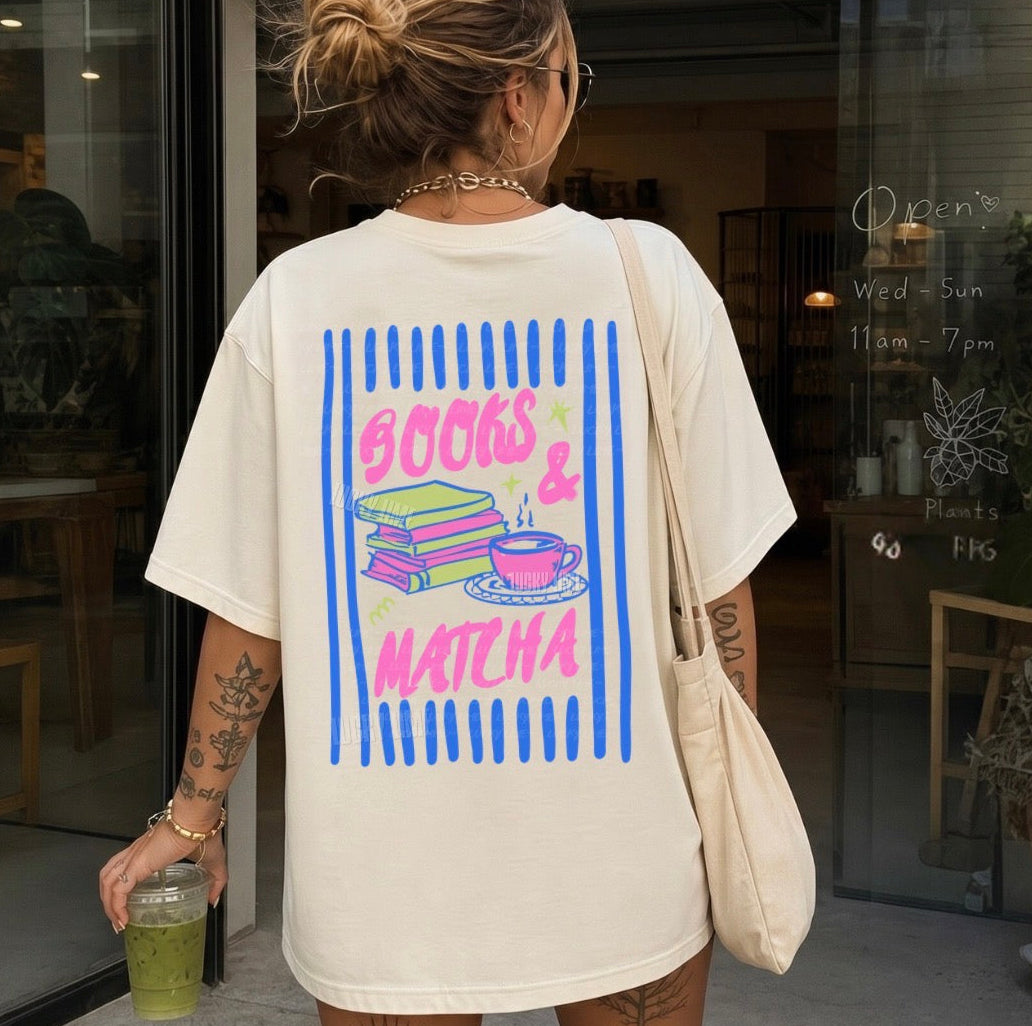 Person wearing a t-shirt with 'Books & Matcha' design, holding a drink, in front of a store.