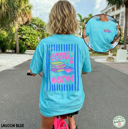 Person wearing a light blue t-shirt with colorful graphics and text, standing outdoors.