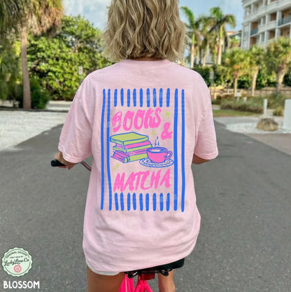 Person wearing a pink t-shirt with 'Books & Matcha' design outdoors.