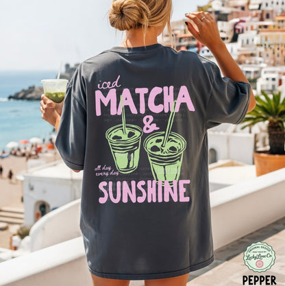 Person wearing a pepper  t-shirt with 'iced matcha & sunshine' text in a scenic location.