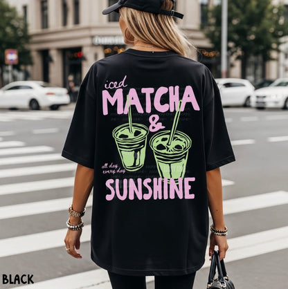 Person wearing a black t-shirt with 'iced matcha & sunshine' text and graphics on a city street.
