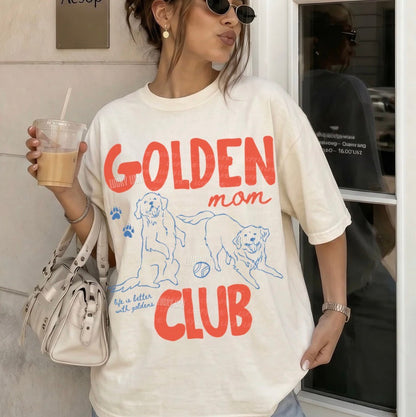 Person wearing a 'Golden Mom Club' t-shirt holding a drink.