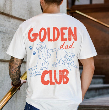 Person wearing a white t-shirt with 'Golden Dad Club' design on the back, standing against a stone wall.