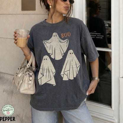 Person wearing a t-shirt with ghost designs and 'BOO' text, holding a drink.