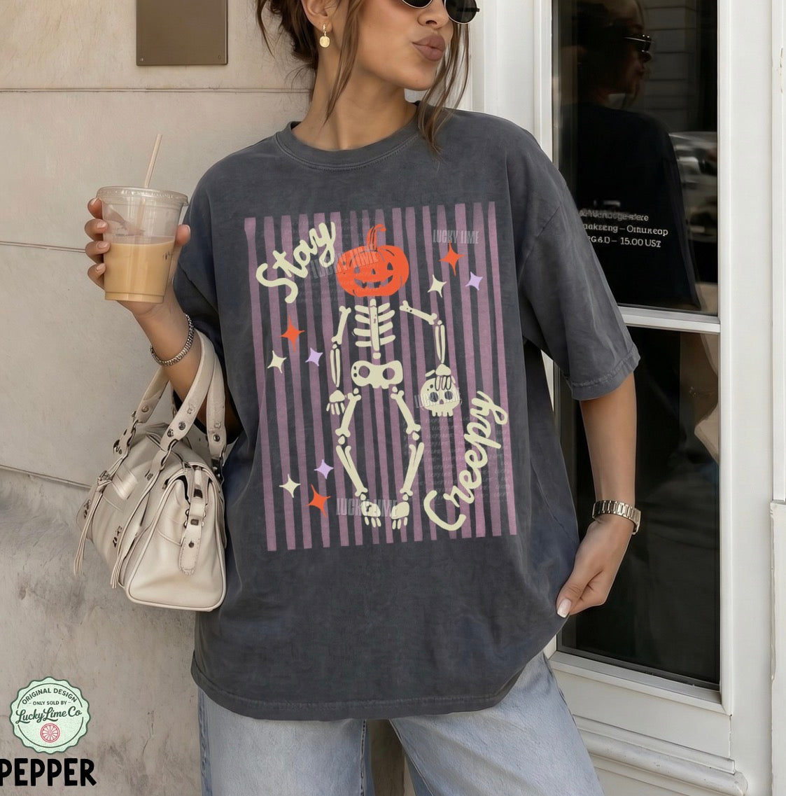 Person wearing a Halloween-themed t-shirt with a skeleton design, holding a drink and a bag.