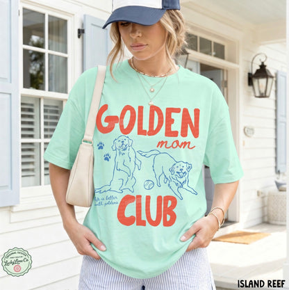 Woman wearing a light green t-shirt with 'Golden Mom Club' text and dog illustrations on a porch.