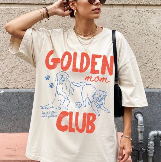 Woman wearing a 'Golden Mom Club' t-shirt against a wall.