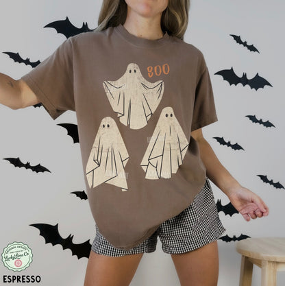 Person wearing a brown t-shirt with ghost designs and checkered shorts, surrounded by black bats on a light gray background.