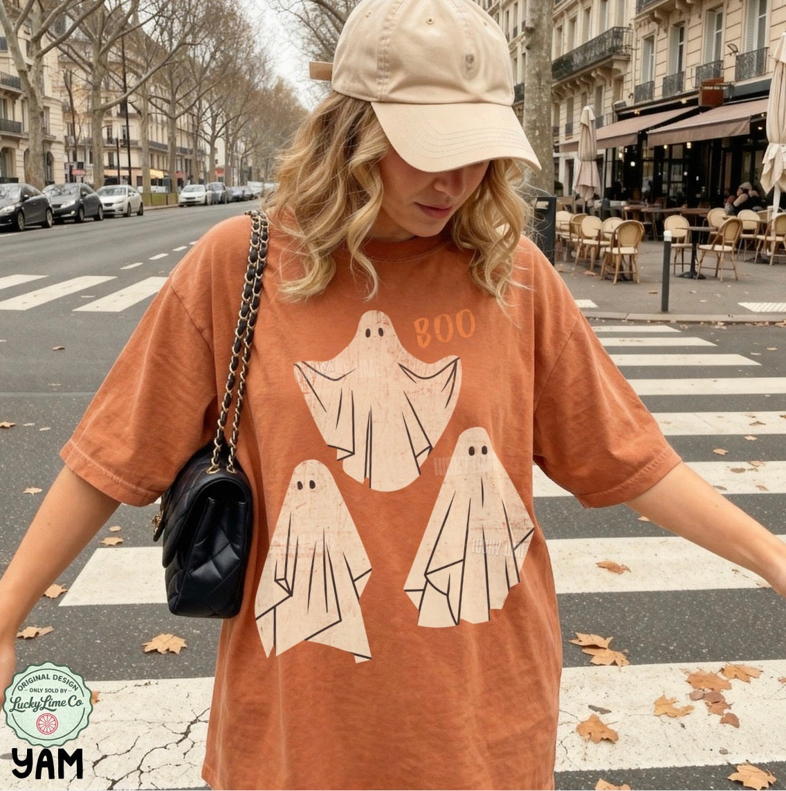Person wearing a t-shirt with ghost designs and the word 'BOO' on a city street.