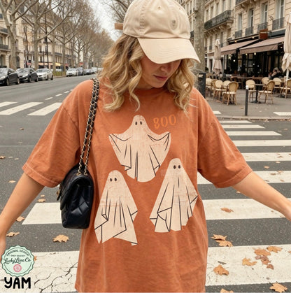 Person wearing a t-shirt with ghost designs and the word 'BOO' on a city street.
